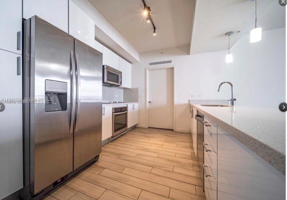 A modern kitchen features stainless steel appliances, white cabinetry, and light wood-look tile flooring — 999 SW 1st Ave # 2105, Miami FL 33130, MIAMI, FL