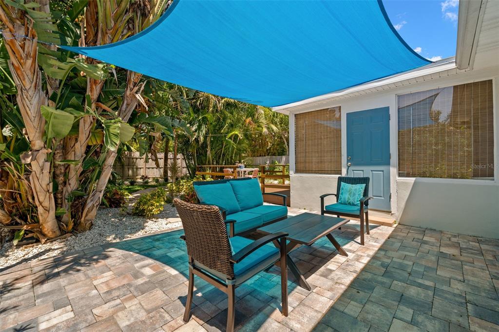 A patio with outdoor furniture sits under a blue shade sail beside a house — 517 79TH AVENUE, ST PETE BEACH, FL