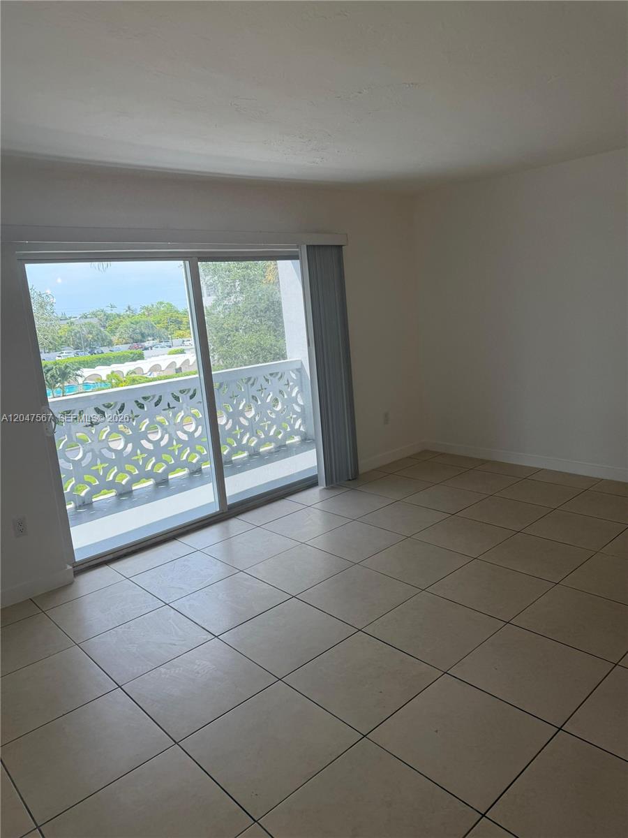 An empty room with beige tile flooring and a sliding glass door leading to a balcony — 2005 Sans Souci Blvd # 305, North Miami FL 33181, NORTH MIAMI, FL