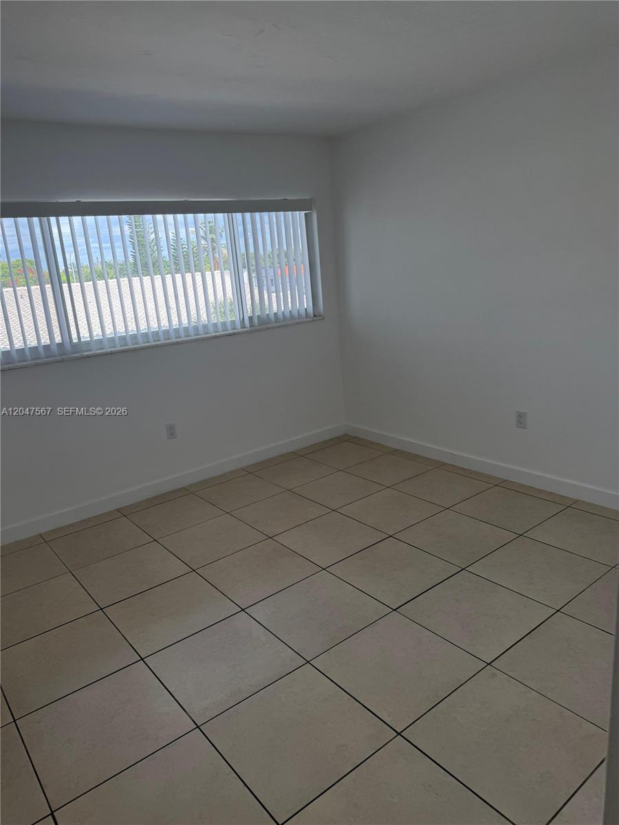 An empty room features light-colored floor tiles, white walls, and a window with vertical blinds — 2005 Sans Souci Blvd # 305, North Miami FL 33181, NORTH MIAMI, FL