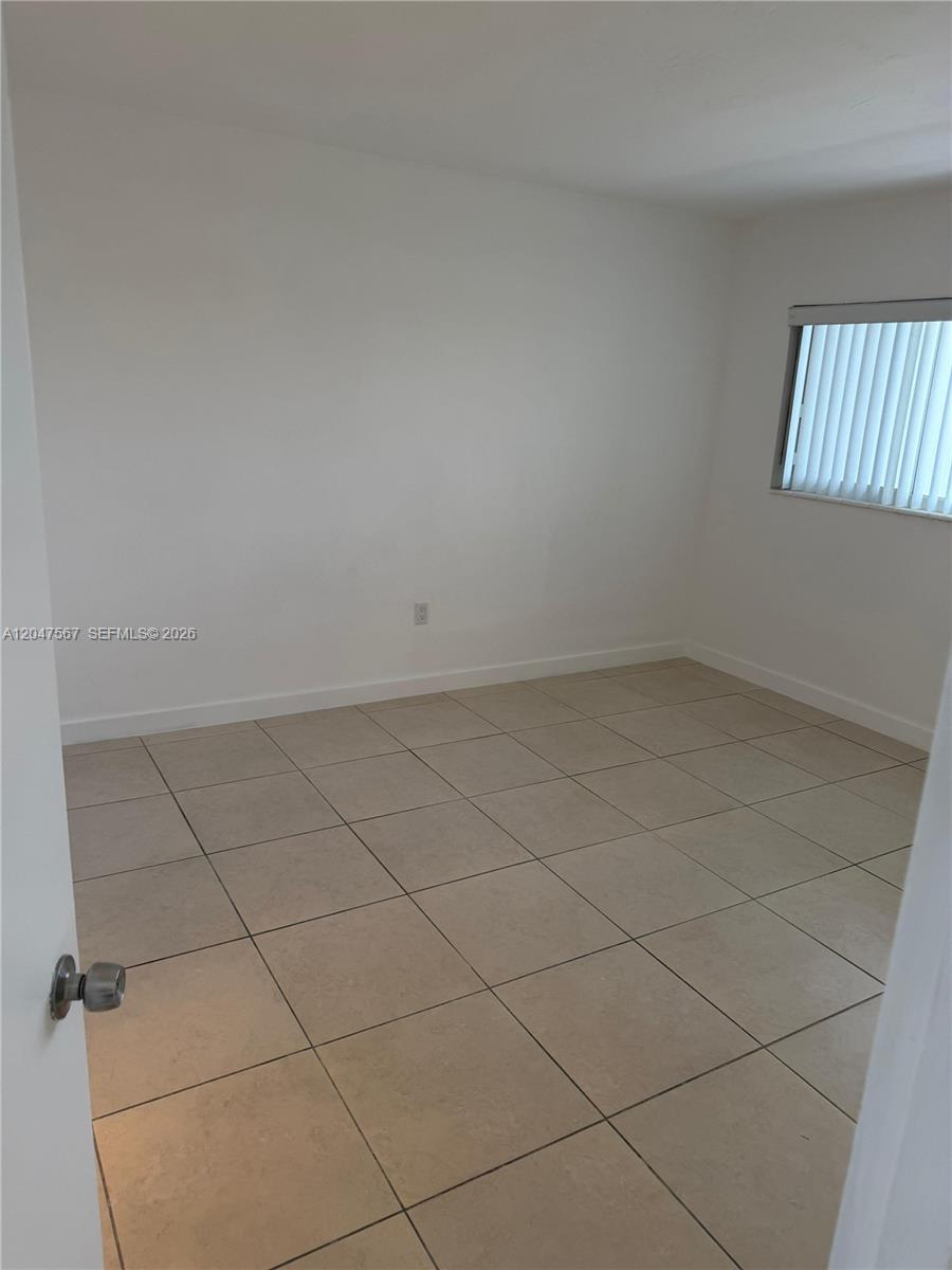 An empty bedroom features white walls, light-colored tile flooring, and a window with vertical blinds — 2005 Sans Souci Blvd # 305, North Miami FL 33181, NORTH MIAMI, FL