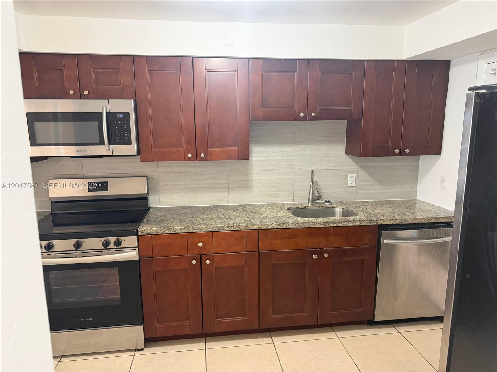 A kitchen features dark wood cabinets, granite countertops, stainless steel appliances, and tile flooring — 2005 Sans Souci Blvd # 305, North Miami FL 33181, NORTH MIAMI, FL
