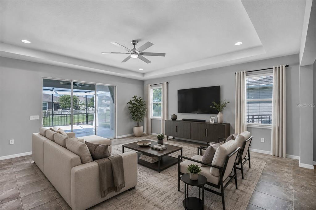 A living room features a tray ceiling, tile floors, a sectional sofa, and sliding glass doors — 32430 BANNACK LANE, WESLEY CHAPEL, FL