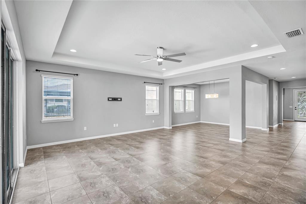 A spacious living area with gray walls, tile flooring, a tray ceiling, and ceiling fan — 32430 BANNACK LANE, WESLEY CHAPEL, FL
