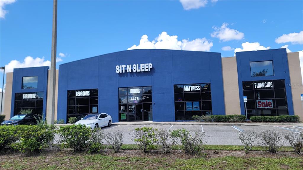 The exterior of a blue commercial building features large glass windows and signage for furniture — 4476 PLEASANT HILL ROAD, KISSIMMEE, FL