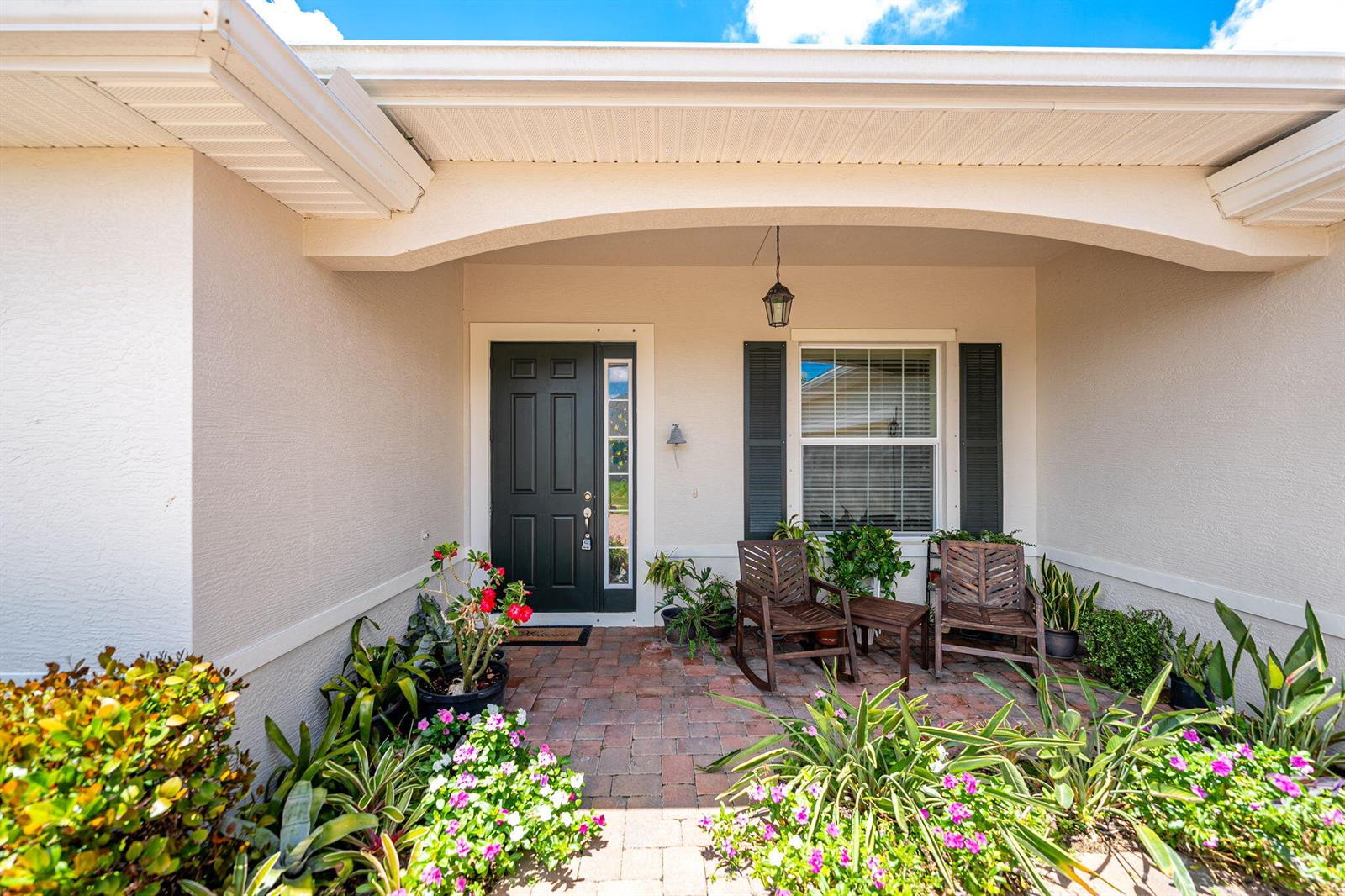 A covered brick porch features a dark front door, a window with shutters, and chairs — 598 Gossamer Wing Way, Sebastian FL 32958, SEBASTIAN, FL