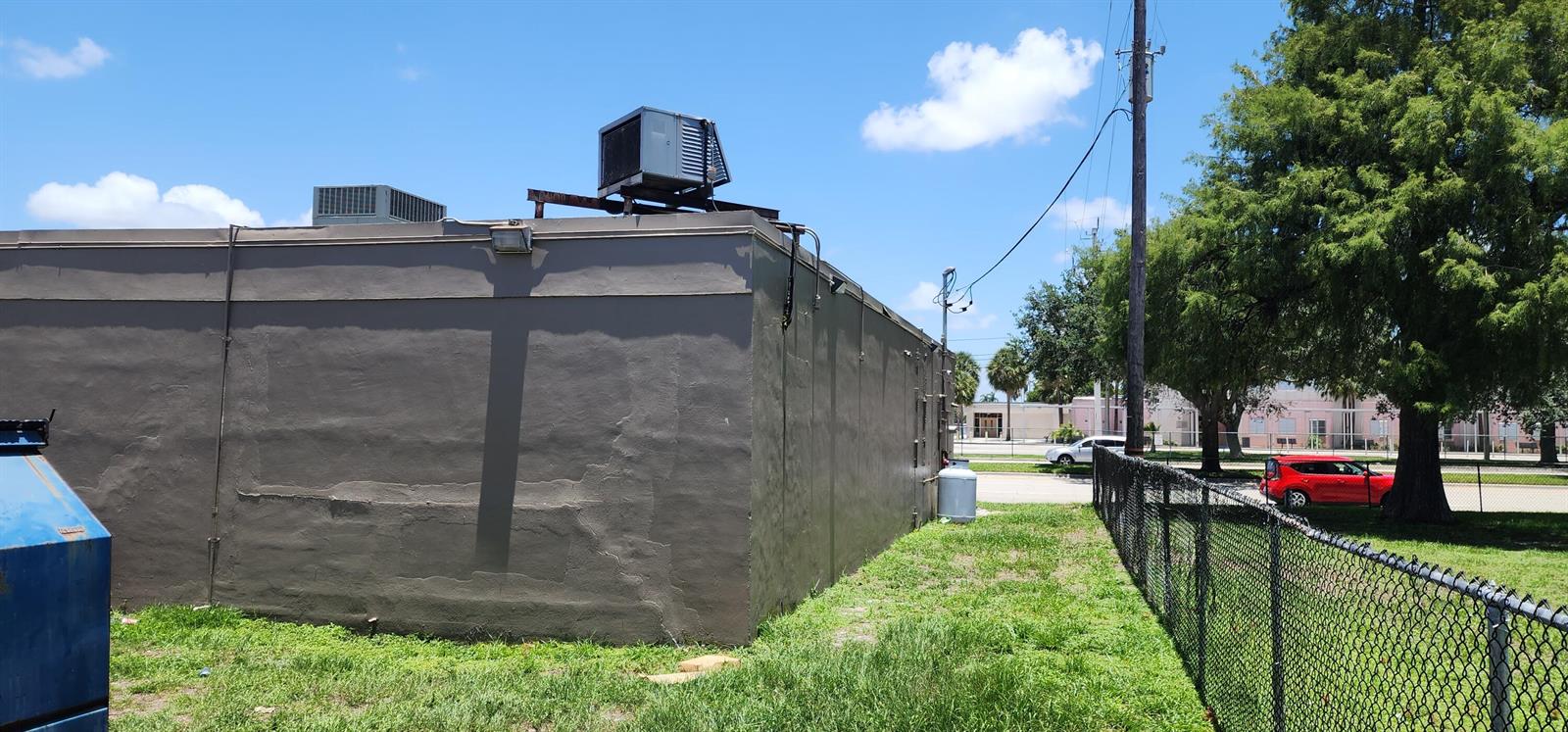 The exterior of a gray commercial building features rooftop HVAC units and a chain-link fence — 430 NW 65th Terrace, Margate FL 33063, MARGATE, FL
