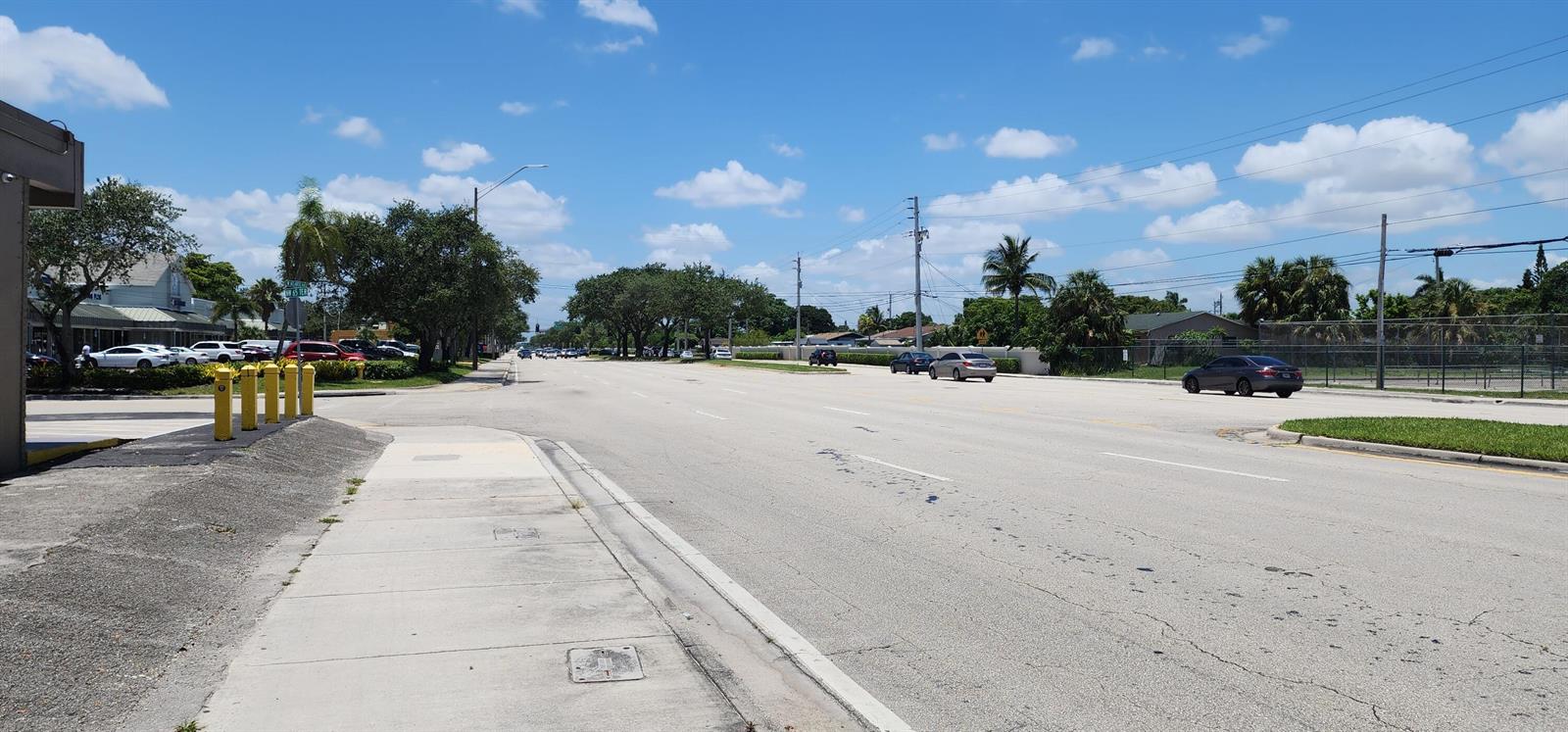 A view of a multi-lane road with a sidewalk, parked cars, and trees under blue skies — 430 NW 65th Terrace, Margate FL 33063, MARGATE, FL