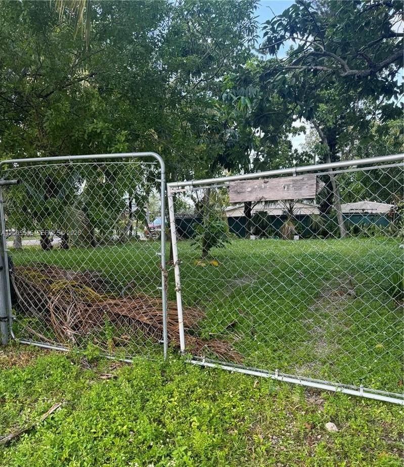 A chain-link gate opens to a grassy, tree-filled lot with a small structure behind — FORT LAUDERDALE, FL