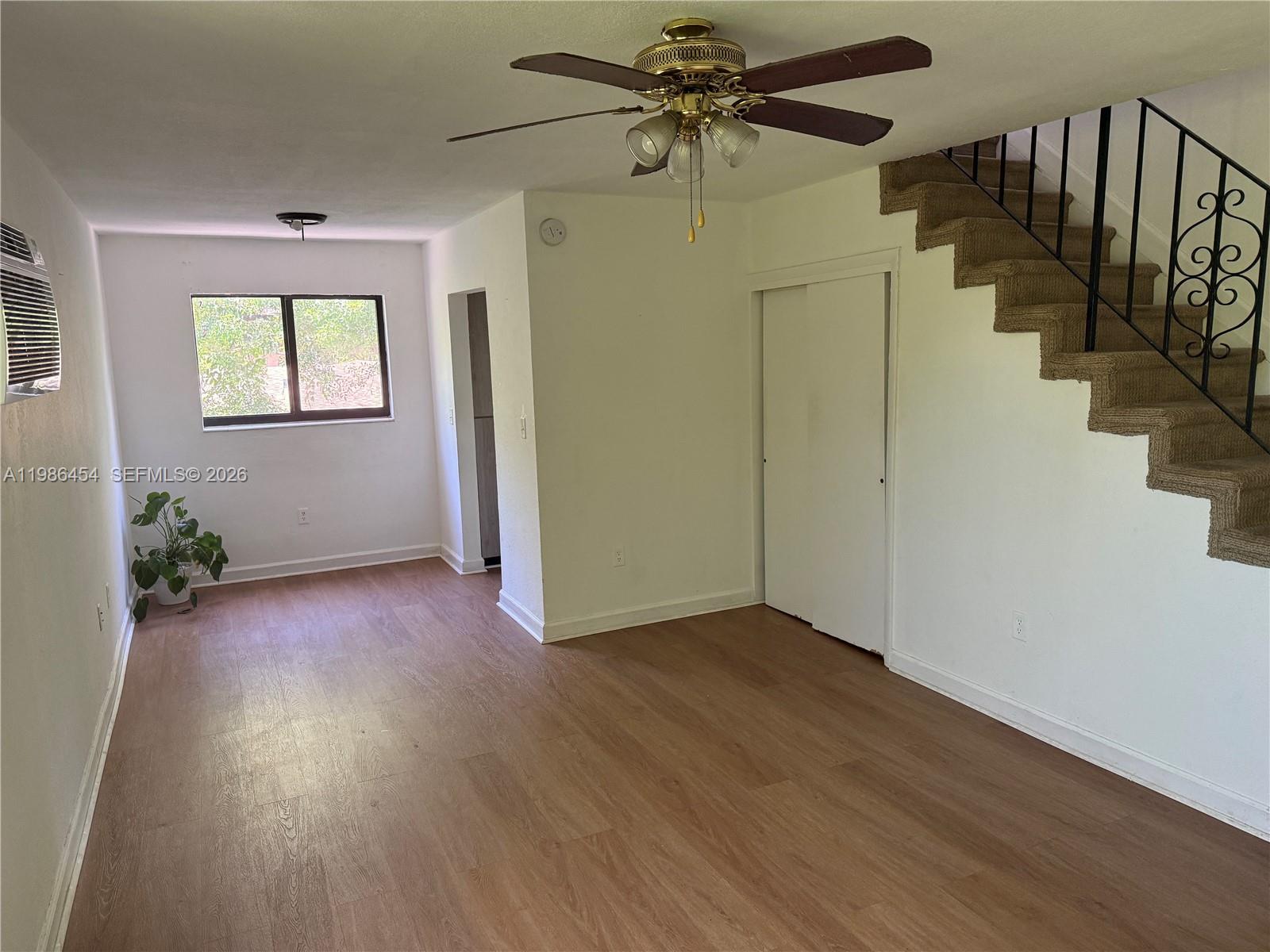 An empty room features wood-look flooring, a staircase with a metal railing, and a ceiling fan — 180 NE 71st St # 3, Miami FL 33138, MIAMI, FL