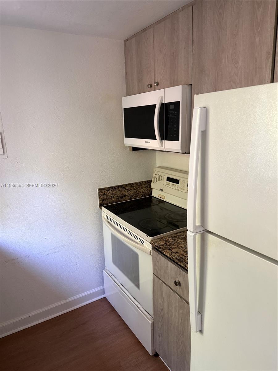 A kitchen sink area features granite countertops, wood-look cabinets, and a window overlooking greenery — 180 NE 71st St # 3, Miami FL 33138, MIAMI, FL