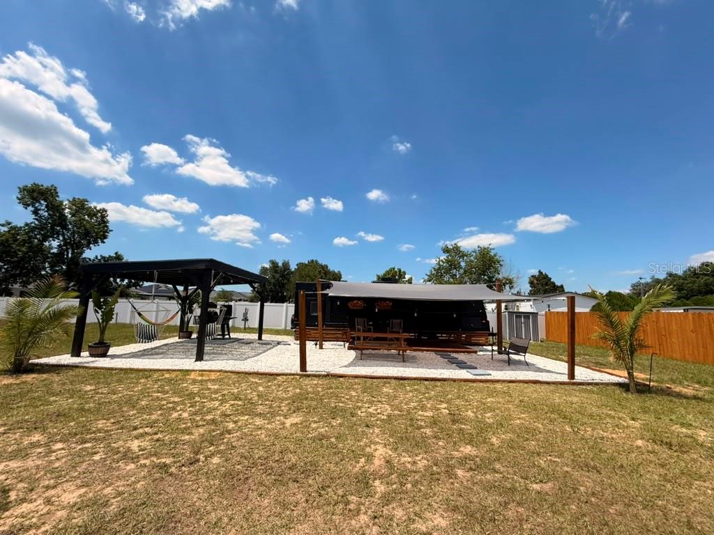 A backyard features a gravel patio with a gazebo, a camper, and a shade sail — 4040 N 10TH STREET, HAINES CITY, FL
