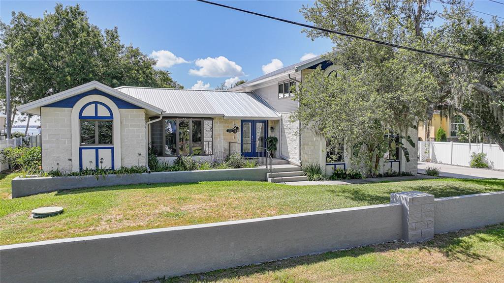 A two-story house with a metal roof, stone facade, and blue trim sits behind a wall — 4460 NORTHSHORE DRIVE, PUNTA GORDA, FL