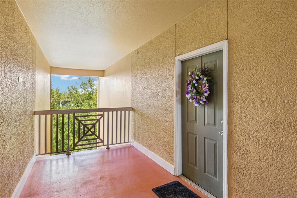 An outdoor apartment entryway features a textured beige wall, a green door with a wreath, and a metal railing — 4207 S DALE MABRY HIGHWAY UNIT 2414, TAMPA, FL