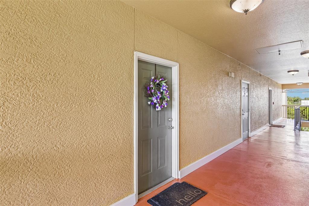 An exterior apartment hallway features textured yellow walls, a grey door with a wreath, and flooring — 4207 S DALE MABRY HIGHWAY UNIT 2414, TAMPA, FL