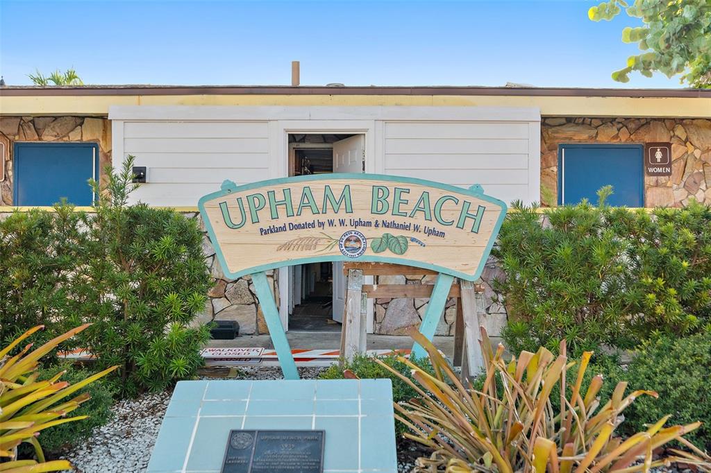 A sign for Upham Beach stands in front of a building with stone exterior walls — 680 71ST AVENUE UNIT 11-A, ST PETE BEACH, FL