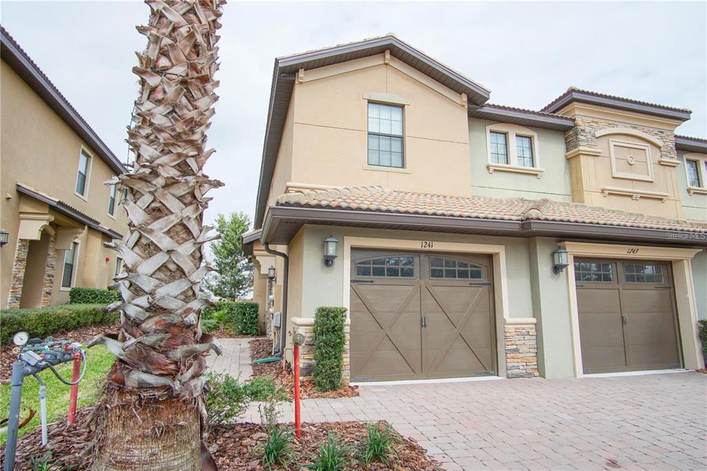 The exterior of a two-story townhouse featuring a tan facade and a brown garage door — 1241 LONG COVE LOOP, DAVENPORT, FL