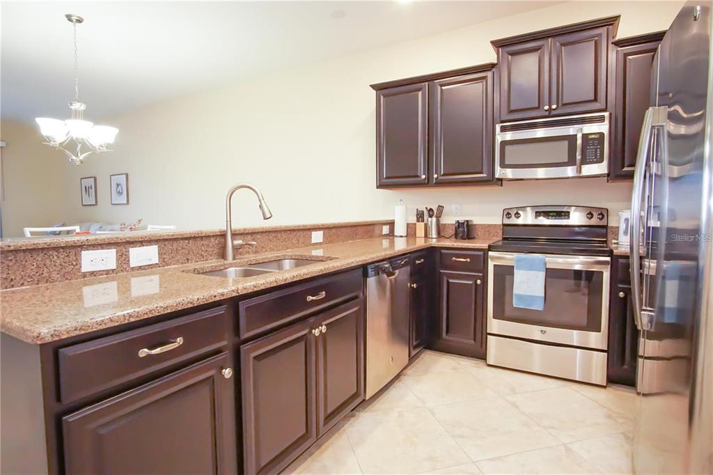 A kitchen features dark wood cabinets, granite countertops, and stainless steel appliances — 1241 LONG COVE LOOP, DAVENPORT, FL