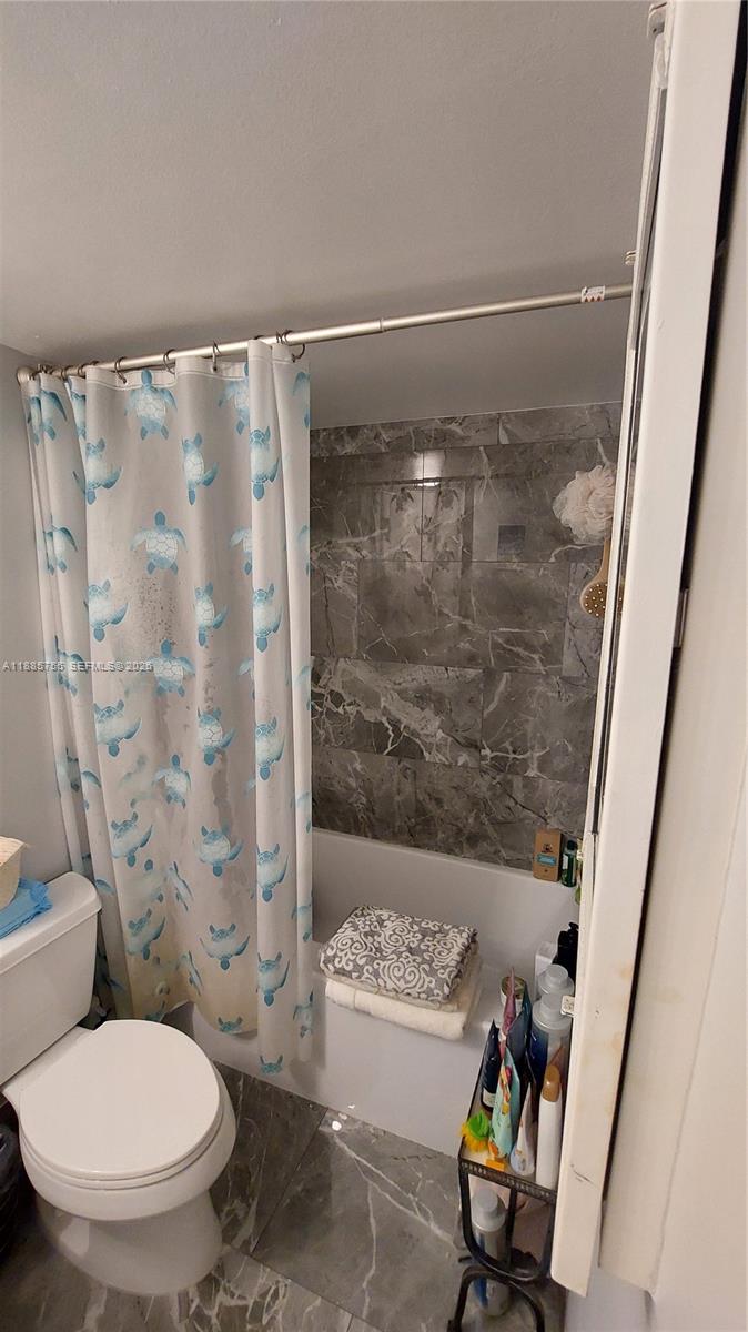 A bathroom features a white toilet, a turtle-patterned shower curtain, and gray marble-look wall tiles — 501 E Three Islands Blvd # 417, Hallandale Beach FL 33009, HALLANDALE BEACH, FL