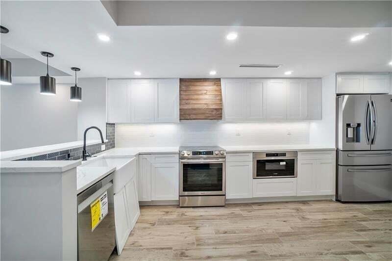 A modern kitchen features white cabinetry, stainless steel appliances, and a wood-paneled range hood — 520 N Ocean Boulevard # 2, Pompano Beach FL 33062, POMPANO BEACH, FL