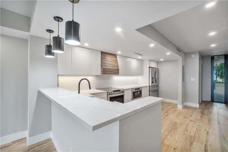 A modern kitchen features white cabinets, a quartz countertop, stainless steel appliances, and pendant lighting — 520 N Ocean Boulevard # 2, Pompano Beach FL 33062, POMPANO BEACH, FL