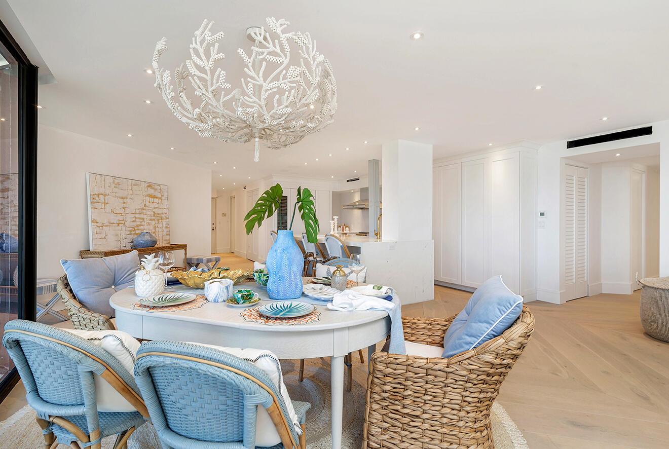 A dining area with a coral-shaped chandelier, wicker chairs, and an open-concept kitchen beyond — 3300 S Ocean Boulevard # 305n, Palm Beach FL 33480, PALM BEACH, FL