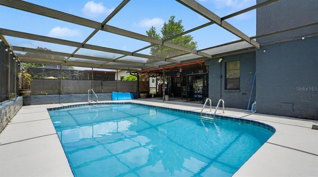 A rectangular swimming pool is enclosed by a screened lanai next to a dark house — 9027 BONNET WAY, WEEKI WACHEE, FL