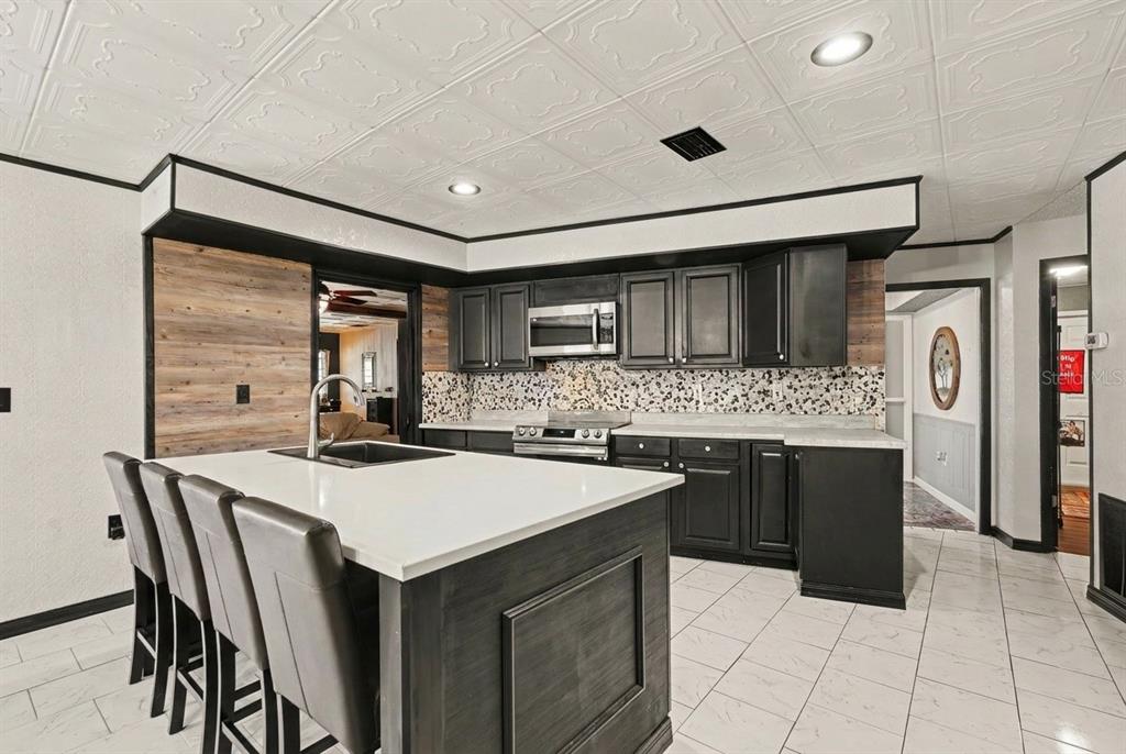A kitchen with a white island, black cabinets, wood-look backsplash, and a white tiled ceiling — 9027 BONNET WAY, WEEKI WACHEE, FL