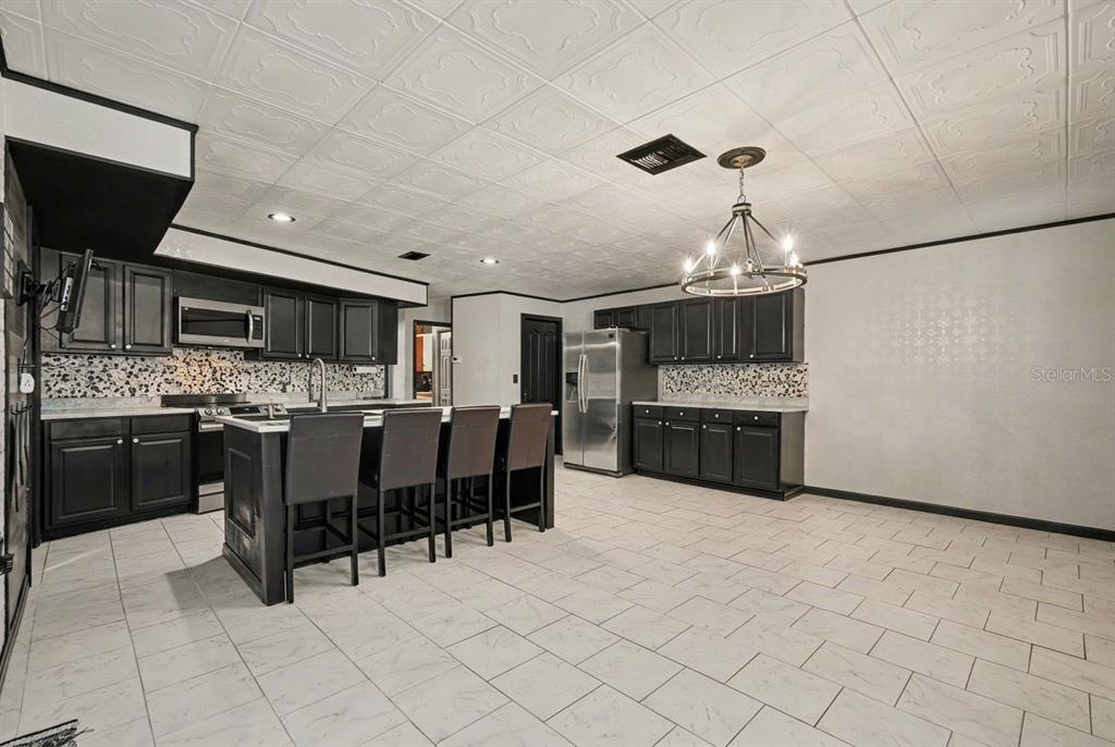 A kitchen features black cabinets, a central island with bar seating, and white tiled flooring — 9027 BONNET WAY, WEEKI WACHEE, FL
