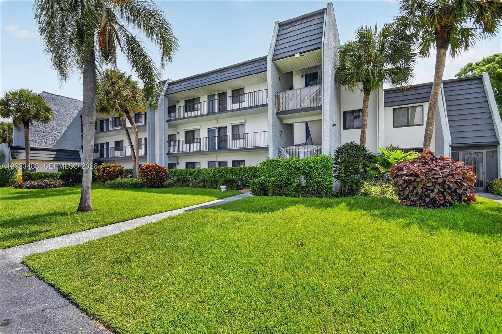 A three-story apartment building exterior features white walls, black railings, and a landscaped lawn — 4230 Deste Ct # 107, Lake Worth FL 33467, LAKE WORTH, FL