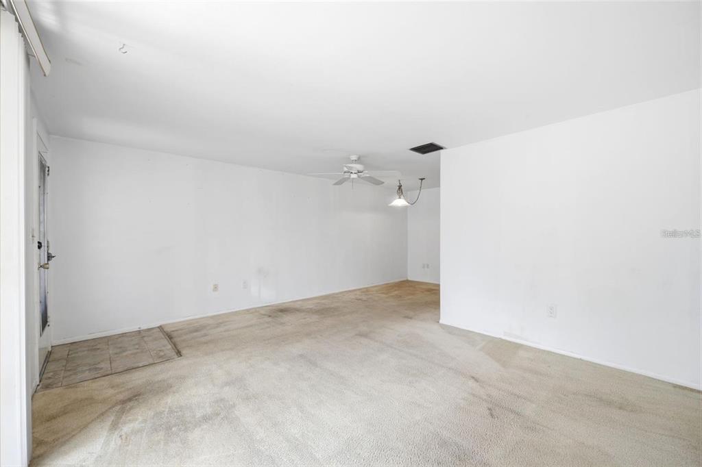An empty living room features white walls, beige carpeting, a ceiling fan, and a light fixture — 4209 TOUCHTON PLACE, NEW PORT RICHEY, FL