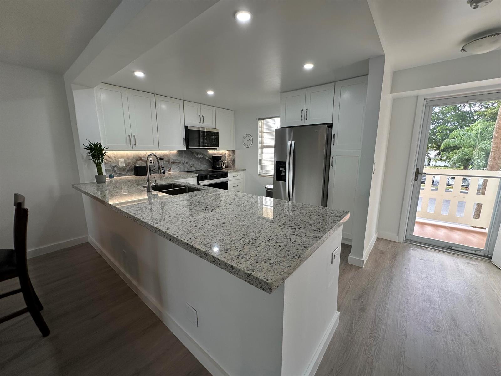 A modern kitchen features white cabinets, granite countertops, stainless steel appliances, and a balcony door — 141 SE 3rd Avenue # 203, Dania Beach FL 33004, DANIA BEACH, FL