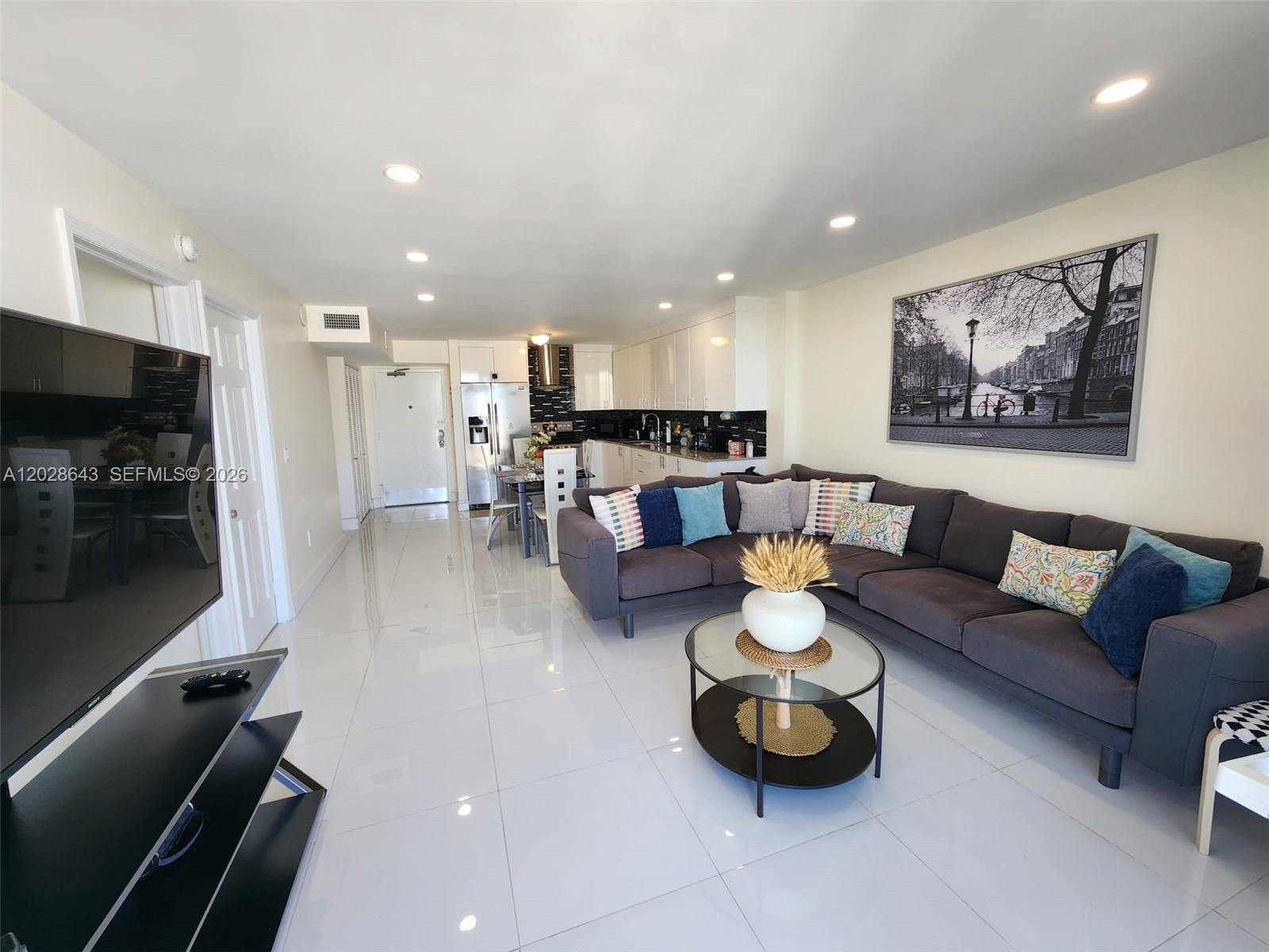 A modern open-concept living room features white tile floors, a dark sectional sofa, and kitchen — 345 Ocean Dr # 602, Miami Beach FL 33139, MIAMI BEACH, FL