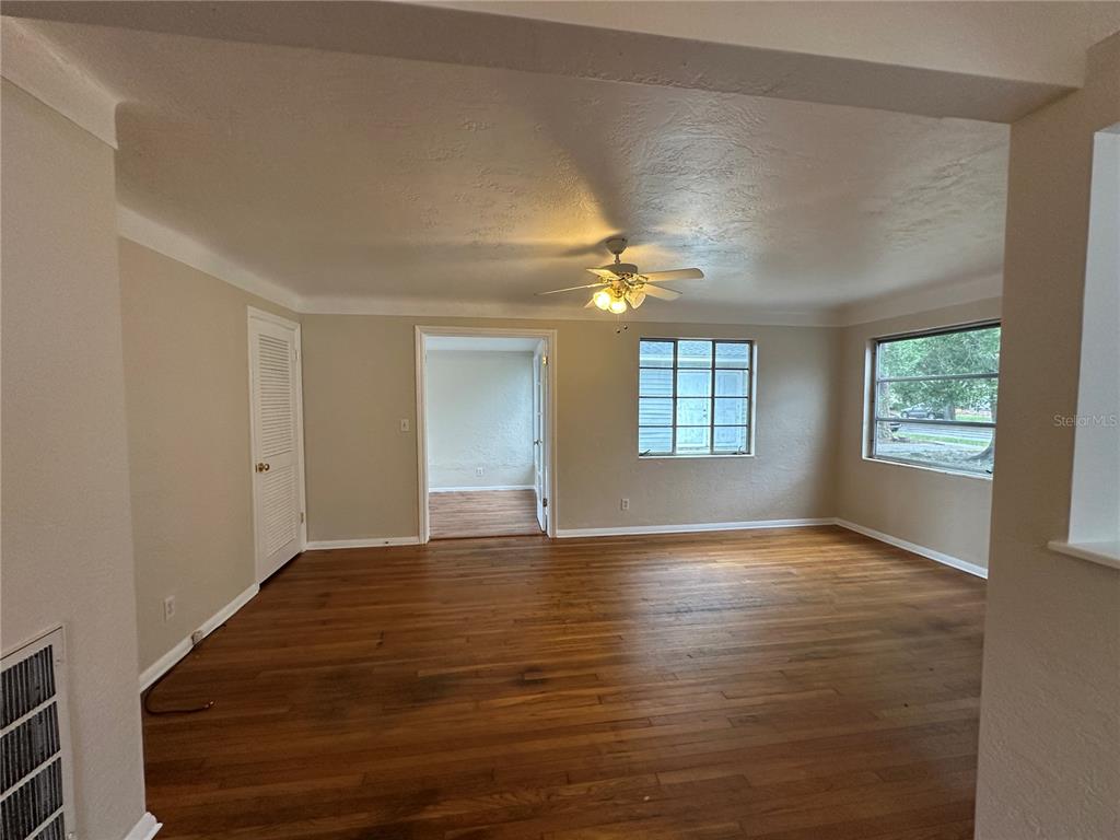 An empty living room features hardwood floors, beige walls, a ceiling fan, and two windows — 4526 6TH AVENUE N, ST PETERSBURG, FL