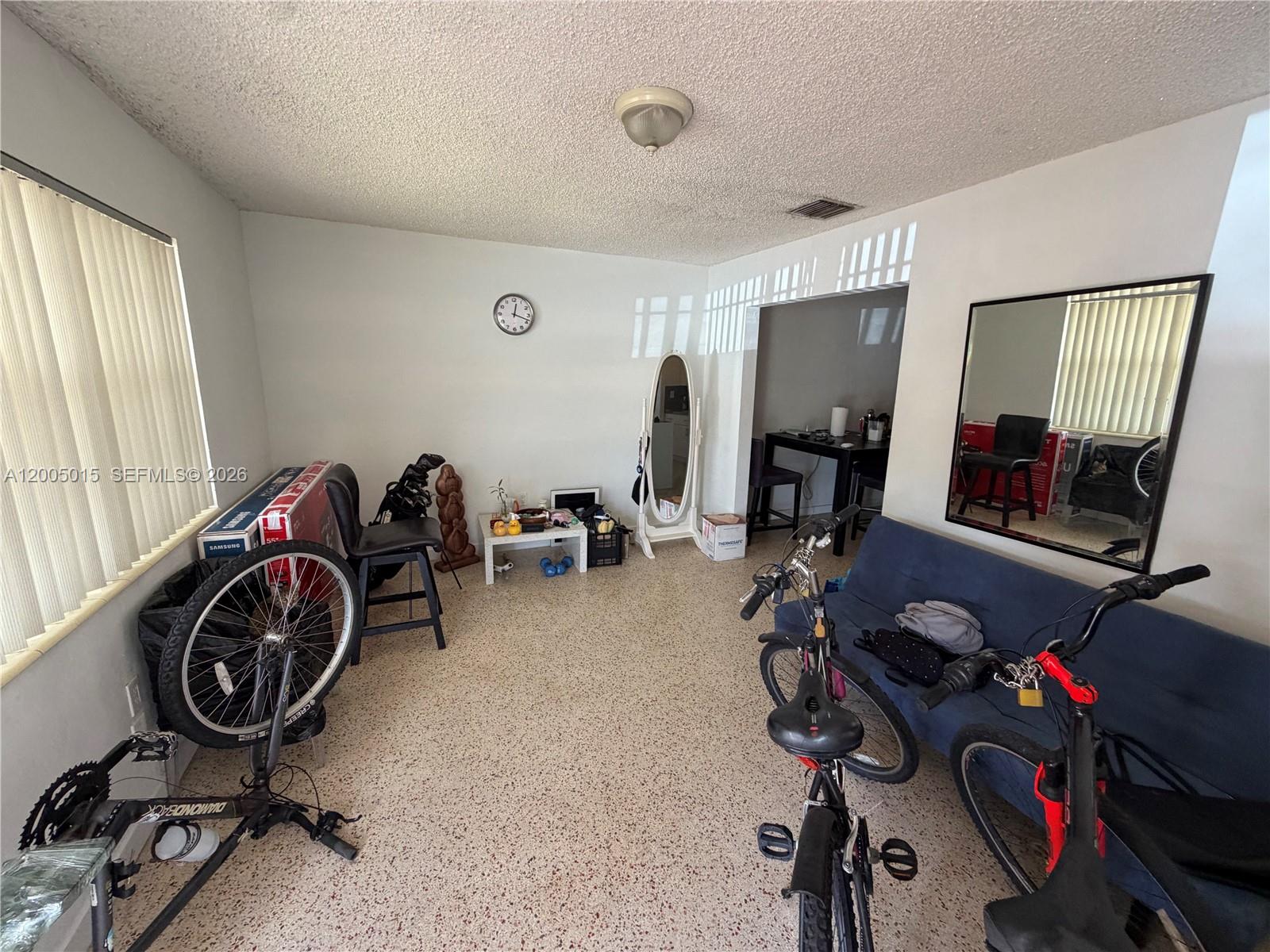 A room with terrazzo flooring, a blue sofa, bicycles, and a large wall mirror — 3361 SW 28th St, Miami FL 33133, MIAMI, FL