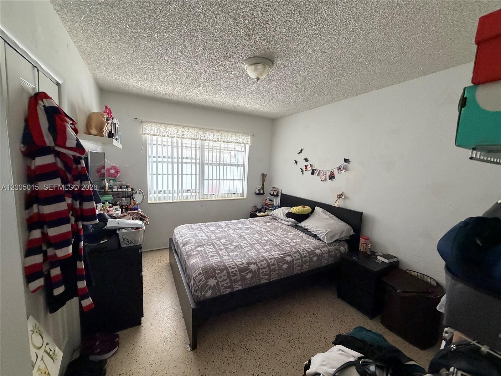 A bedroom features a bed with patterned bedding, a window with blinds, and speckled flooring — 3361 SW 28th St, Miami FL 33133, MIAMI, FL