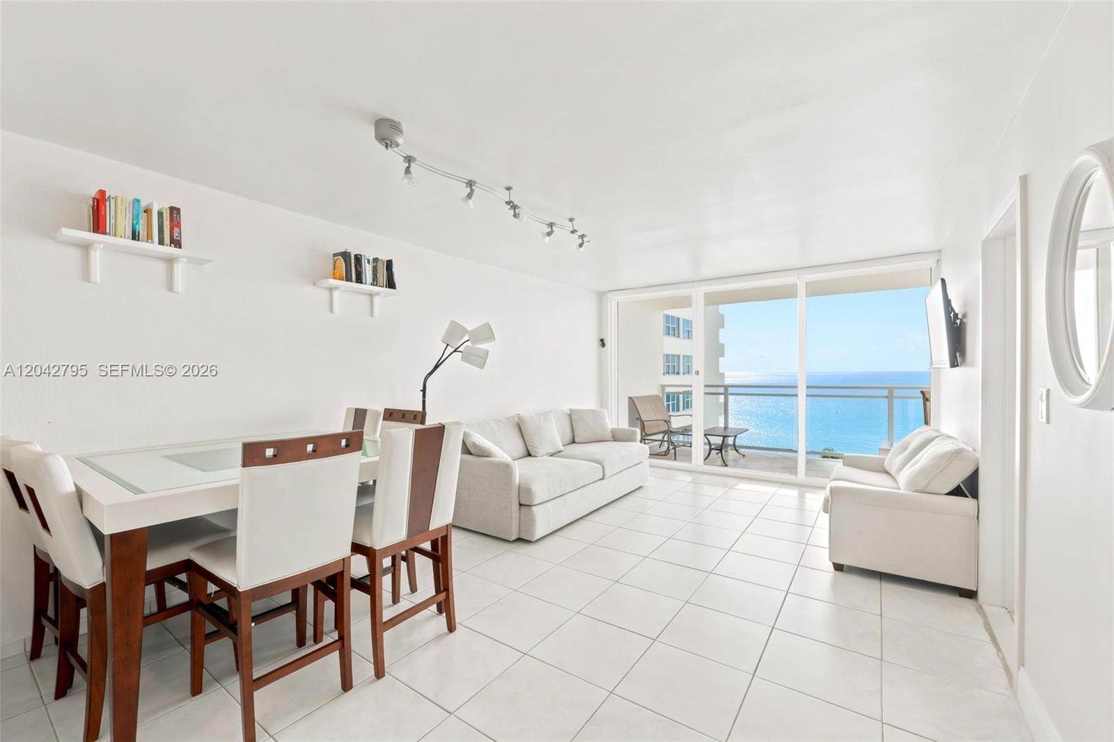 A bright living and dining area features white tile floors and a balcony overlooking the ocean — 2030 S Ocean Dr # 816, Hallandale Beach FL 33009, HALLANDALE BEACH, FL