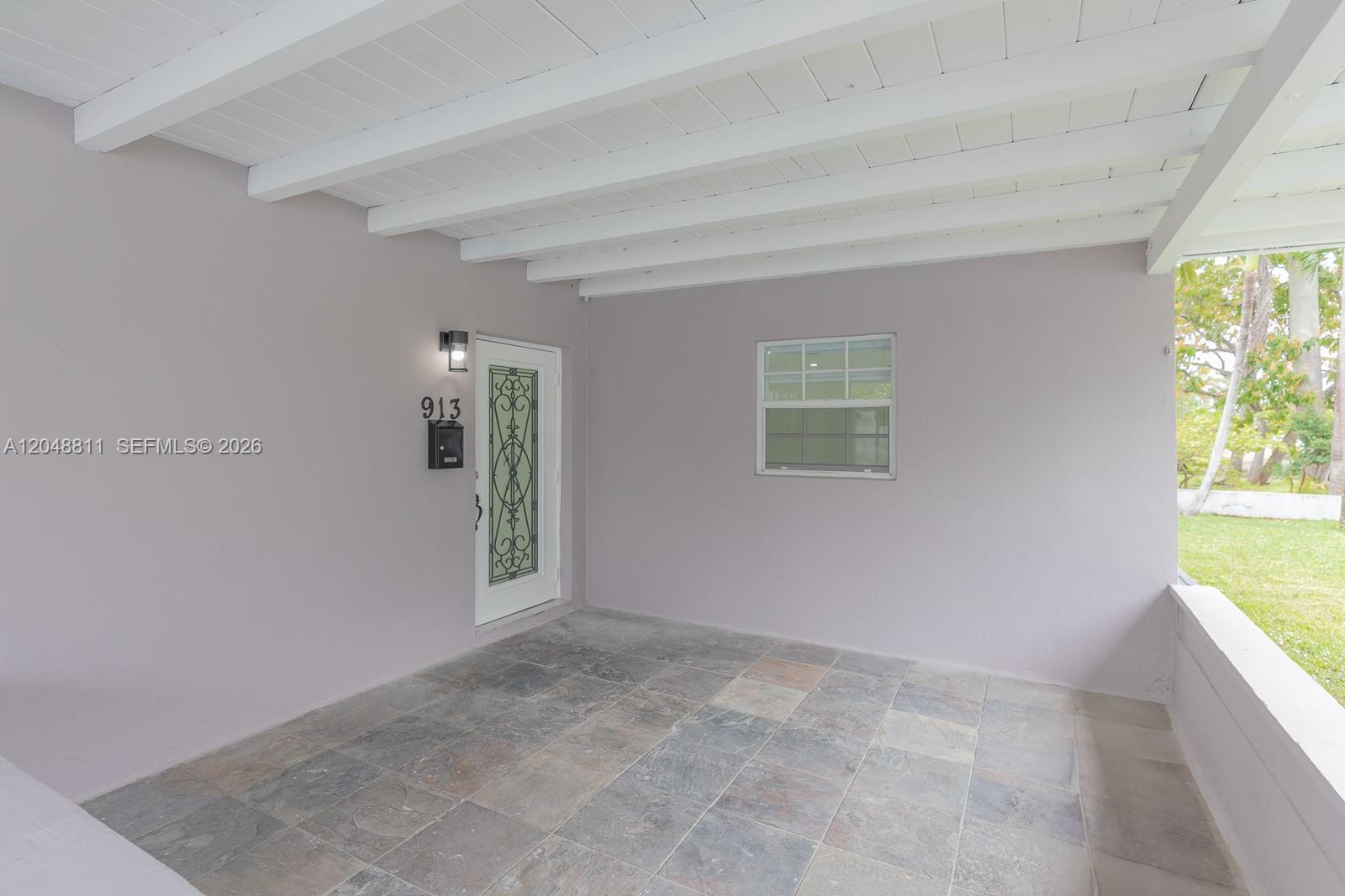 A covered porch features a tiled floor, a white door with decorative glass, and a window — 913 NE 2nd St, Hallandale Beach FL 33009, HALLANDALE BEACH, FL