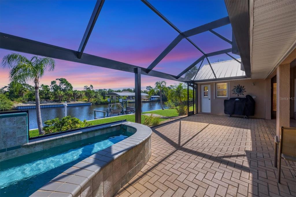 A screened-in patio features a raised tiled spa overlooking a canal at sunset — 13564 WAINWRIGHT DRIVE, PORT CHARLOTTE, FL