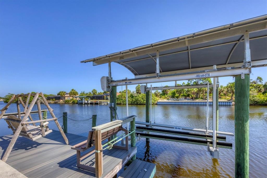 A wooden dock features a swing, a bench, and a covered boat lift over water — 13564 WAINWRIGHT DRIVE, PORT CHARLOTTE, FL