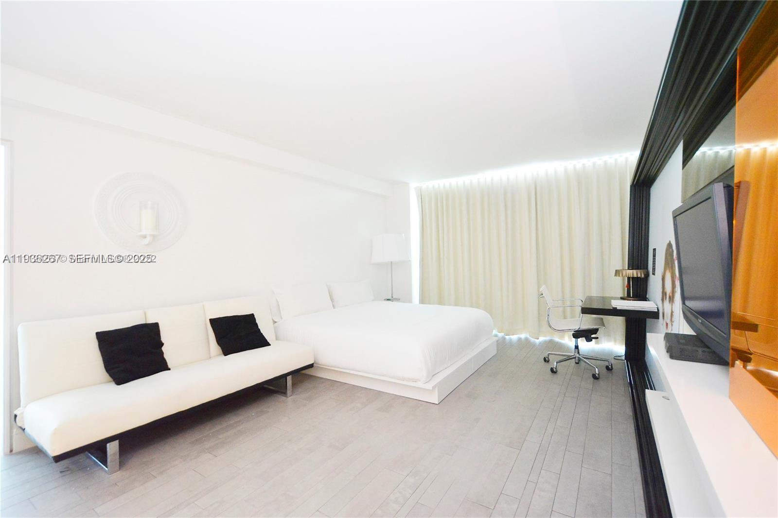 A modern hotel-style bedroom features a white bed, a white sofa, and a desk — 1100 West Ave # 1220, Miami Beach FL 33139, MIAMI BEACH, FL