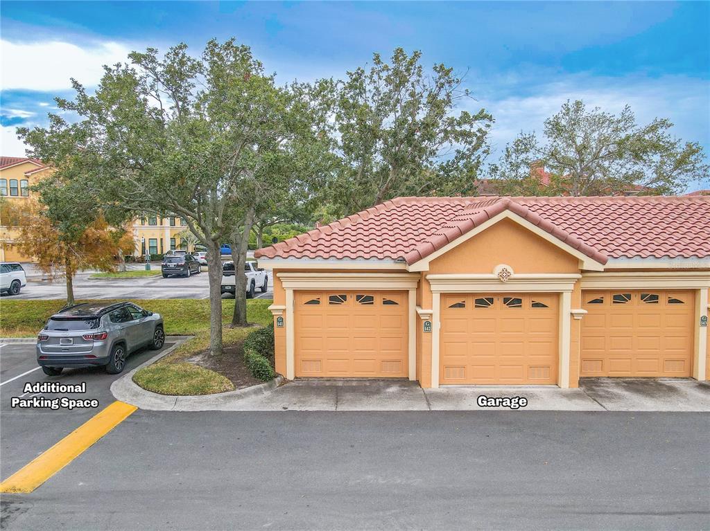 A row of three tan garage doors is situated next to an outdoor parking space — 2738 VIA TIVOLI UNIT 220B, CLEARWATER, FL