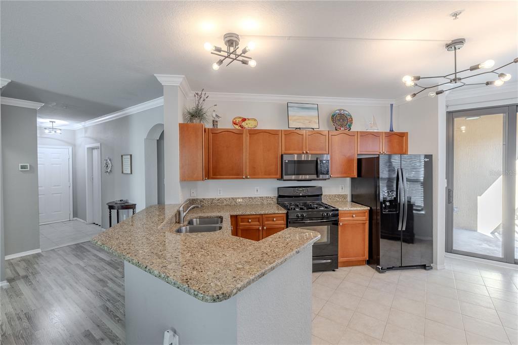 A kitchen features wood cabinets, granite countertops, black appliances, and a breakfast bar — 2738 VIA TIVOLI UNIT 220B, CLEARWATER, FL