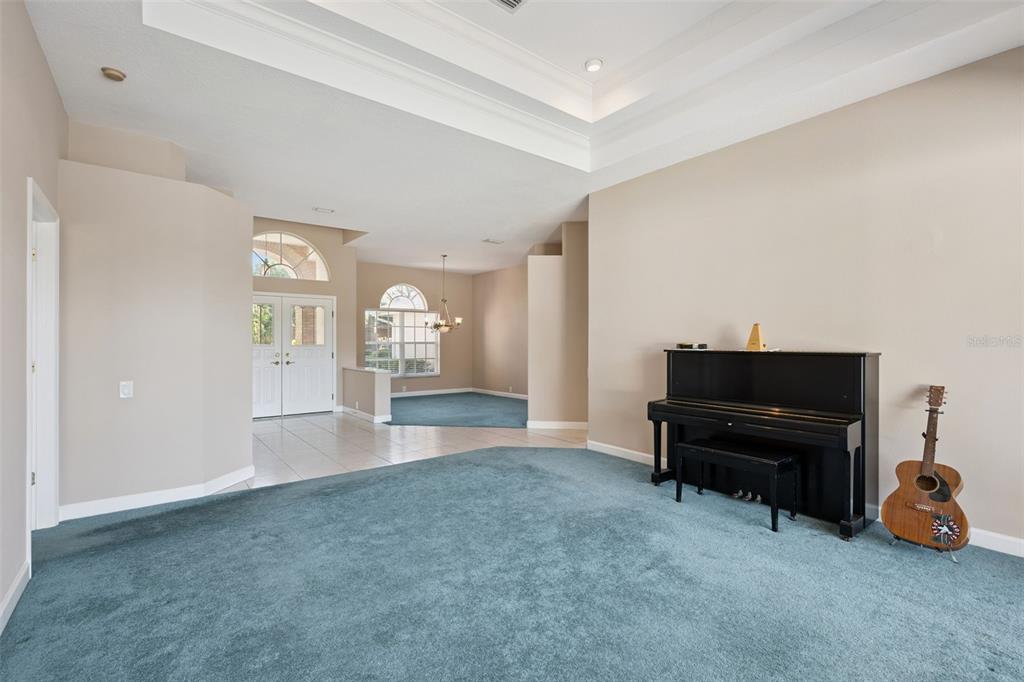 A living room features teal carpeting, a black upright piano, and a guitar — 3833 SANIBEL COVE, OVIEDO, FL