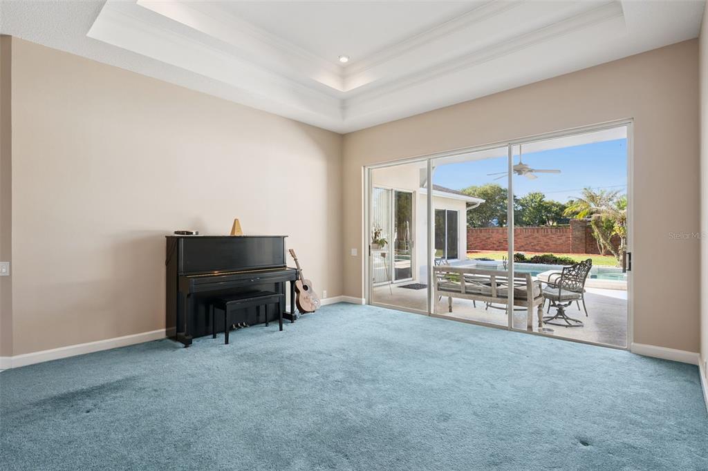 A room with blue carpet, a black piano, and sliding glass doors opening to a pool — 3833 SANIBEL COVE, OVIEDO, FL