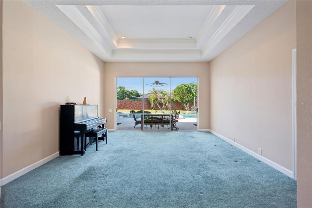 A living room with blue carpet, a black piano, and sliding doors opening to a pool — 3833 SANIBEL COVE, OVIEDO, FL