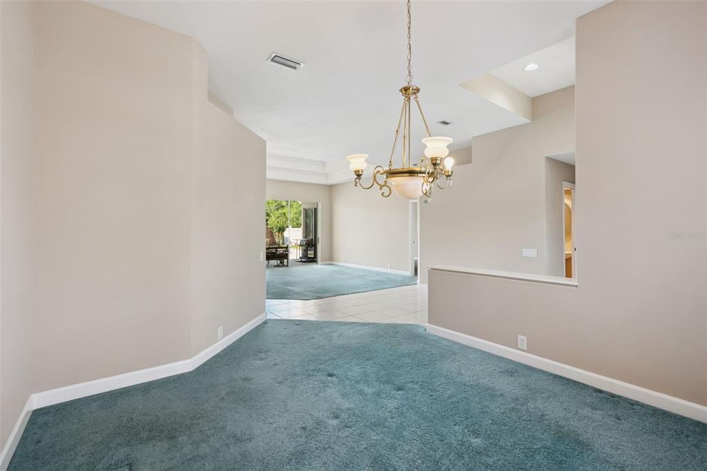 A dining area with teal carpeting and a chandelier overlooks a tiled living space — 3833 SANIBEL COVE, OVIEDO, FL