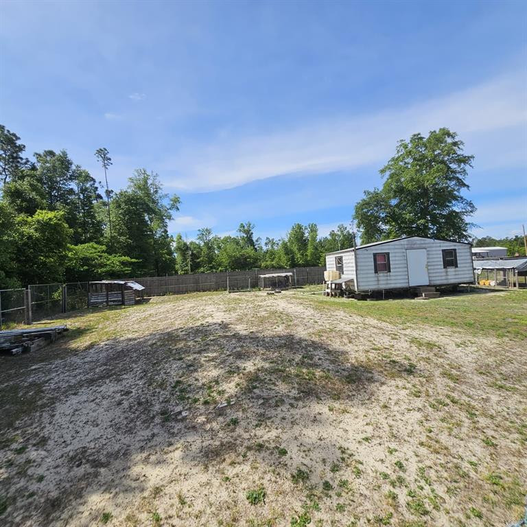 A small mobile home sits on a sandy, fenced lot with scattered trees and structures — 12132 PINERIDGE ROAD, FOUNTAIN, FL