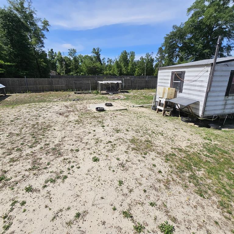 A sandy backyard features a small white shed, a concrete pad, and a wooden fence — 12132 PINERIDGE ROAD, FOUNTAIN, FL