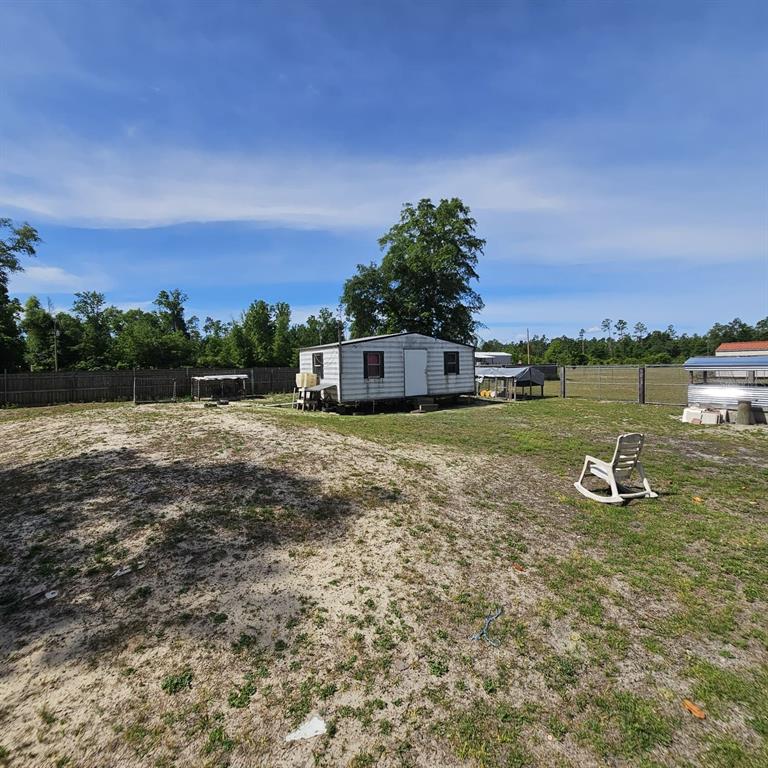 A small, weathered mobile home sits in a large, grassy, fenced-in yard — 12132 PINERIDGE ROAD, FOUNTAIN, FL